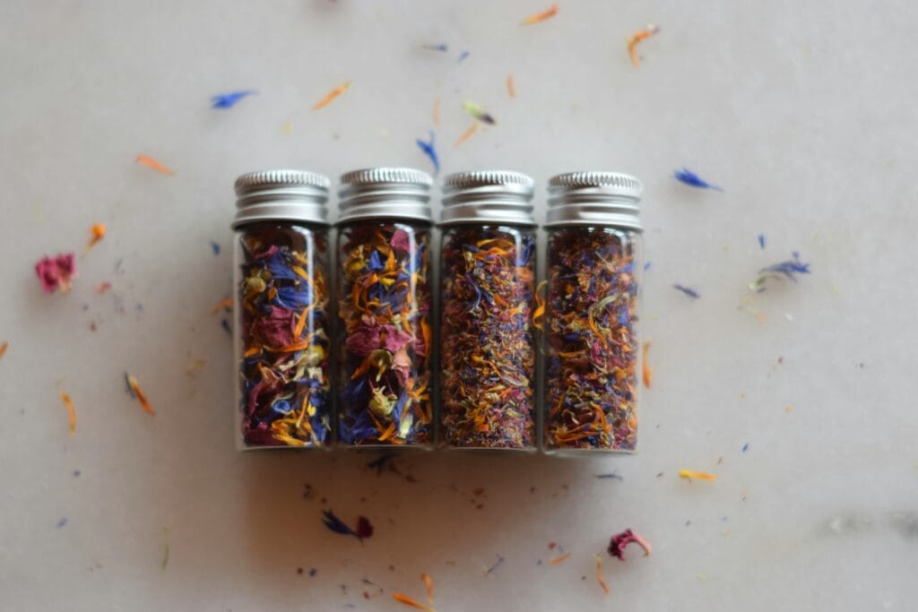 Four small bottles filled with dried colorful flower petals